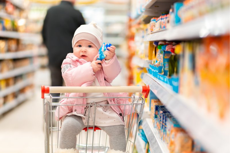 Baby in a supermarket trolley holding a food pouch. Copyright: IStock