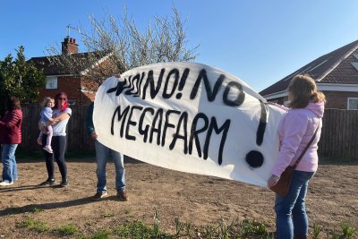 Activists in Methwold hold up white banner with black writing that says: NO! NO! NO MEGAFARM!. Credit: Lily O'Mara