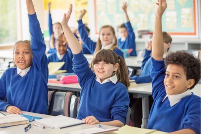 School children wearing blue school uniforms raising hands in classroom.. Copyright: Caiaimage/Chris Ryan | istock