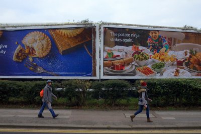 People walking by in front of large billboards advertising Christmas food and groceries. Copyright: Thinglass | Shutterstock