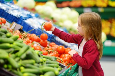Little girl choosing tomatoes in a food store or a supermarket. Copyright: MNStudio | shutterstock