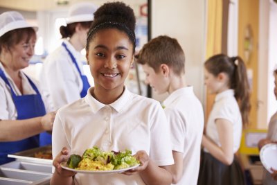 A young girl holding a plate of food in the school canteen. Credit: Monkey Business Images | Shutterstock
