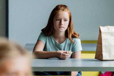 Girl with sandwhich sits alone in school canteen . Credit: LightField Studios | Shutterstock